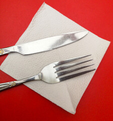 Knife and fork in a white napkin on a red