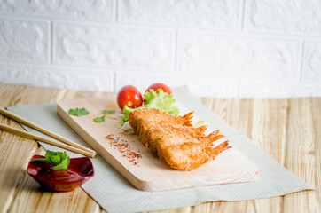 Butterfly ebi furai shrimp served with tomato and lettuce on a wooden chopping board along with ketchup