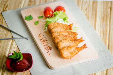 Butterfly ebi furai shrimp served with tomato and lettuce on a wooden chopping board along with ketchup