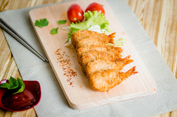 Butterfly ebi furai shrimp served with tomato and lettuce on a wooden chopping board along with ketchup