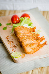 Butterfly ebi furai shrimp served with tomato and lettuce on a wooden chopping board along with ketchup