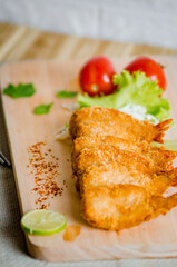 Butterfly ebi furai shrimp served with tomato and lettuce on a wooden chopping board along with ketchup