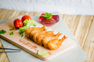 Butterfly ebi furai shrimp served with tomato and lettuce on a wooden chopping board along with ketchup