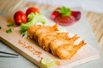 Butterfly ebi furai shrimp served with tomato and lettuce on a wooden chopping board along with ketchup