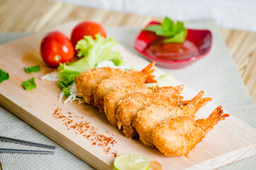 Butterfly ebi furai shrimp served with tomato and lettuce on a wooden chopping board along with ketchup