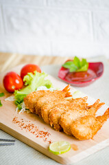 Butterfly ebi furai shrimp served with tomato and lettuce on a wooden chopping board along with ketchup