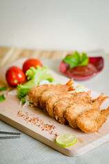 Butterfly ebi furai shrimp served with tomato and lettuce on a wooden chopping board along with ketchup