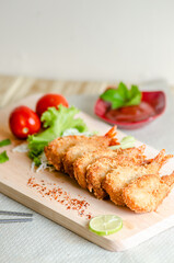 Butterfly ebi furai shrimp served with tomato and lettuce on a wooden chopping board along with ketchup