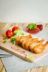 Butterfly ebi furai shrimp served with tomato and lettuce on a wooden chopping board along with ketchup