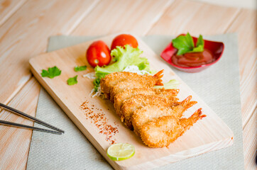 Butterfly ebi furai shrimp served with tomato and lettuce on a wooden chopping board along with ketchup