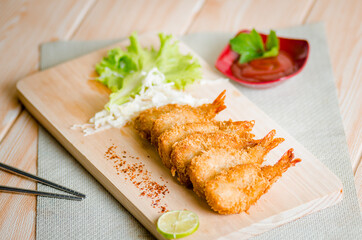 Butterfly ebi furai shrimp served with tomato and lettuce on a wooden chopping board along with ketchup