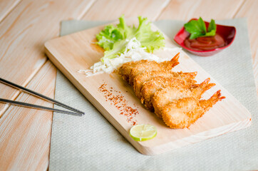 Butterfly ebi furai shrimp served with tomato and lettuce on a wooden chopping board along with ketchup