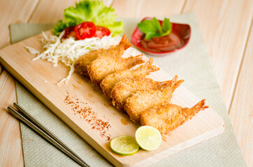 Butterfly ebi furai shrimp served with tomato and lettuce on a wooden chopping board along with ketchup