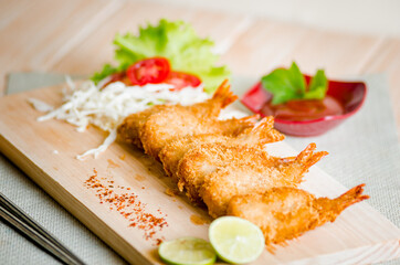 Butterfly ebi furai shrimp served with tomato and lettuce on a wooden chopping board along with ketchup