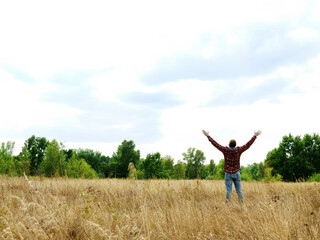 Naklejka na ściany i meble A man in an autumn field stretches out his hands to the sky.