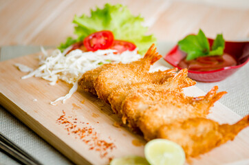 Butterfly ebi furai shrimp served with tomato and lettuce on a wooden chopping board along with ketchup