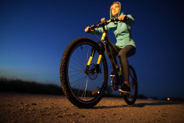 Fototapeta na wymiar Young woman cycling on bicycle at countryside road at the night