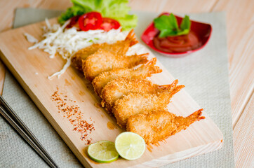 Butterfly ebi furai shrimp served with tomato and lettuce on a wooden chopping board along with ketchup