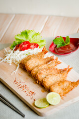 Butterfly ebi furai shrimp served with tomato and lettuce on a wooden chopping board along with ketchup