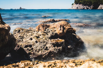Fototapeta na wymiar Long exposure sea waves crash with splashes on large coastal stones - rocky coast