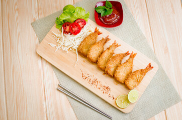 Butterfly ebi furai shrimp served with tomato and lettuce on a wooden chopping board along with ketchup