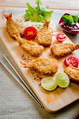 Butterfly ebi furai shrimp served with tomato and lettuce on a wooden chopping board along with ketchup