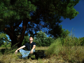 Fototapeta premium Male tourist meditates while sitting under a tree in the forest.