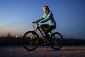 Fototapeta na wymiar Young woman cycling on bicycle at countryside road at the night