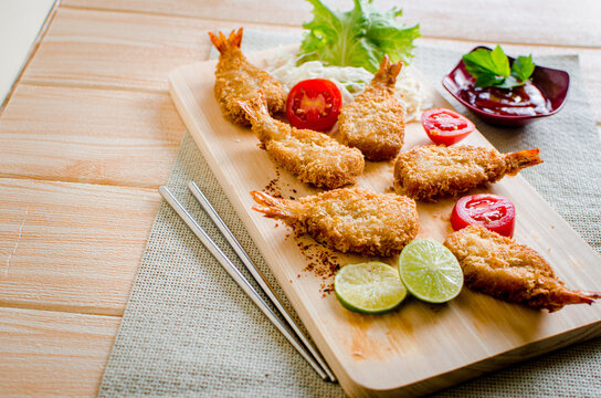 Butterfly ebi furai shrimp served with tomato and lettuce on a wooden chopping board along with ketchup