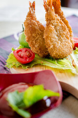 Butterfly ebi furai shrimp served with tomato and lettuce on a wooden chopping board along with ketchup
