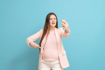 Fototapeta premium frightened young pregnant woman on blue background calls by mobile phone, discharge of amniotic fluid, the beginning of labor process, video link
