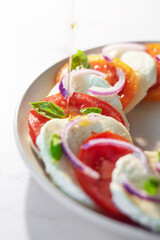 Home prepared italian well known salad caprese with tomatoes, mozzarella, red onion and basil