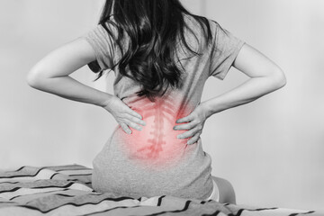 Backache and Lower back pain concept. Woman touching lower back at pain point, on bed after waking...