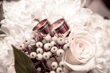 Wedding rings lie on a bouquet of white roses