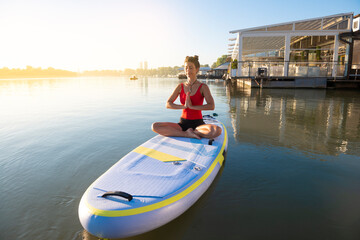 Woman meditating and practising yoga in a seiza position during sunrise in paddle board
