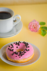 Pink round donut at bright yellow background with coffee glass
