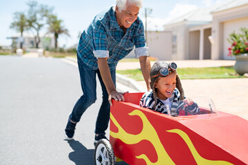 Grandfather pushing his little boy on toy car - obrazy, fototapety, plakaty