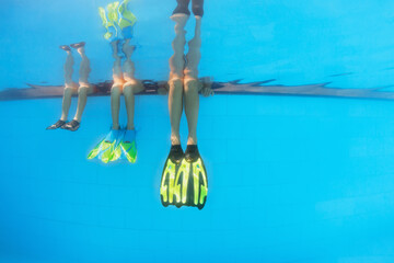 Happy people have fun at pool side edge. Funny photo of mother with kids legs in fins in aqua park...