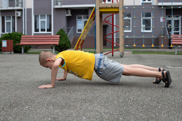 7-year-old blond boy in a bright yellow t-shirt doing push-UPS on the Playground in the courtyard...