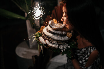 Portrait of charming girl blowing on candles on birthday cake surrounded by friends at party