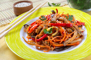 Korean eggplants. Spicy vegetable salad with eggplant, bell peppers, carrots, onions on a plate on a bright background.