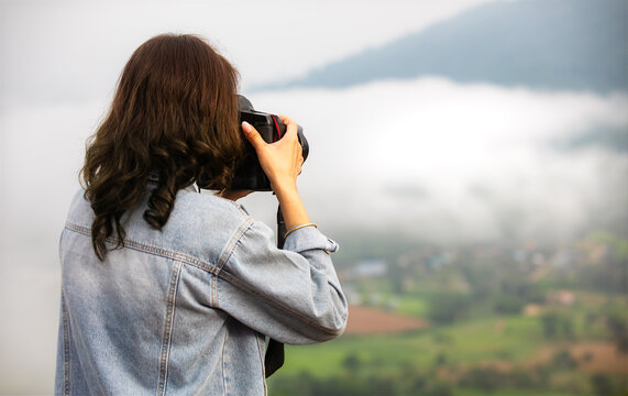 Nature female photographer traveler taking landscape photos of a high green mountain in the morning with white soft fog blur in background. Idea for the tourist lifestyle in outdoor life.