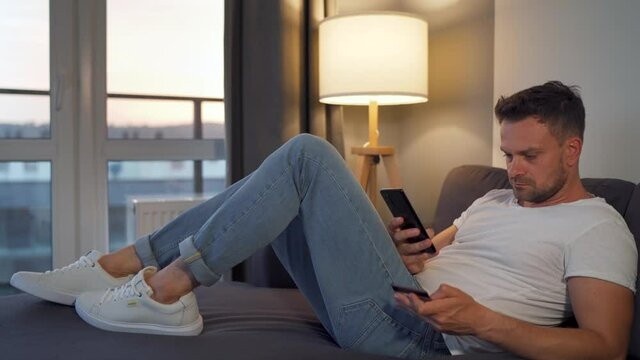 Man lying on the couch in a cozy room and makes an online purchase using a credit card and her smartphone. Online shopping, lifestyle technology.