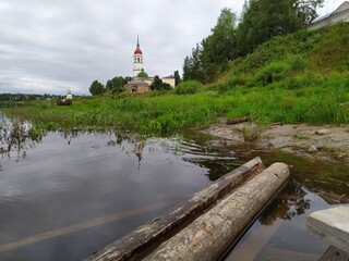 Landscape with wet logs in river water and old church on the shore