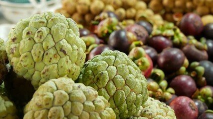 Assorted exotic fruits on stall in market. Bunch of sugar apples placed on blurred background of longans and mangosteens on stall on market in tropical country