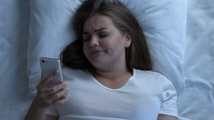 Sad overweight girl reading message about break up after bad date lying in bed