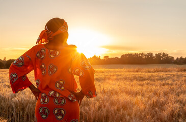 African woman in traditional clothes standing in a field of crops at sunset or sunrise - 377859109