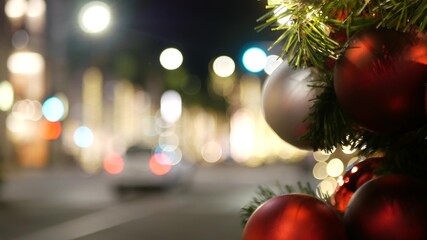 Closeup of Festively Decorated Outdoor Christmas tree with bright red balls on blurred sparkling fairy background. Defocused garland lights, Bokeh effect. Defocused night city street with cars on road