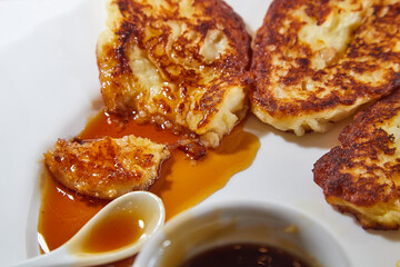 Pancakes on white plate and sweet liquid honey or caramel with a small spoon and with background. Delicious fried flour food. Unhealthy and harmful, but very tasty food.