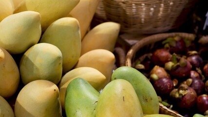Fruits and vegetables on rustic stall. Assorted fresh ripe fruits and vegetables placed on rustic oriental stall in market. Green and yellow mango and mangosteens in basket.